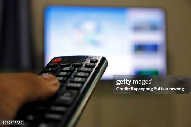 hand holding remote control of television. man watching tv at home and using remote control. - parte de una serie fotografías e imágenes de stock