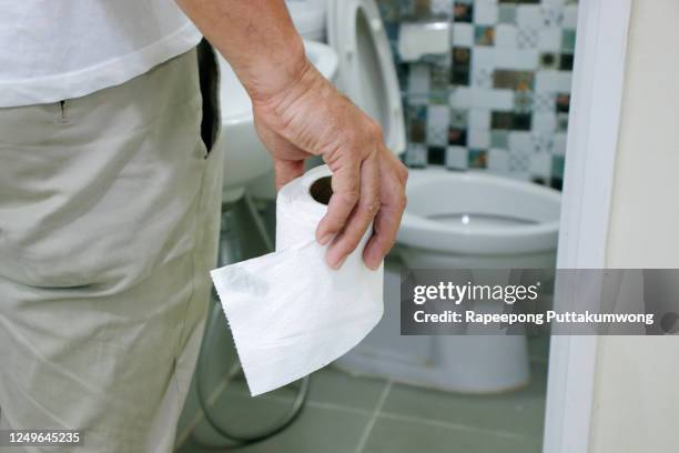 man holding toilet tissue roll in bathroom - diarrhö stock-fotos und bilder