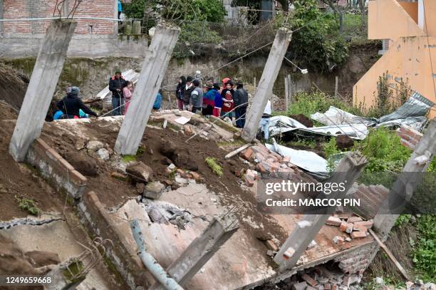 People stand next to a destroyed house after a landslide in Alausi, Ecuador, on March 27, 2023. - At least 7 people have died, and 46 other are still...