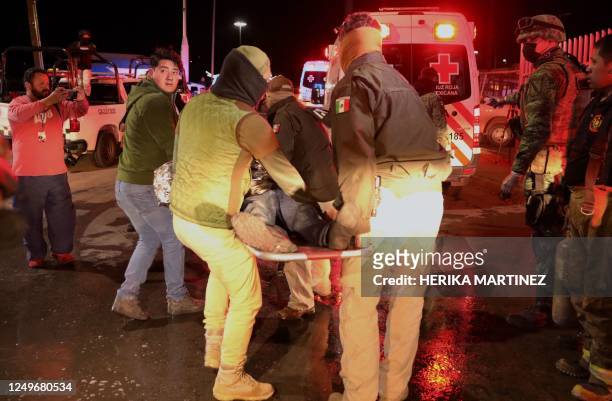 Police officers carry an injured migrant following a fire that killed dozens of migrants, in the immigration station in Ciudad Juarez, Chihuahua...