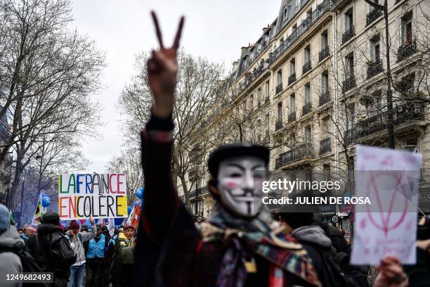 Protester holds a placard reading "France in anger" as another wearing a Guy Fawkes mask gestures the V-sign during a demonstration after the...