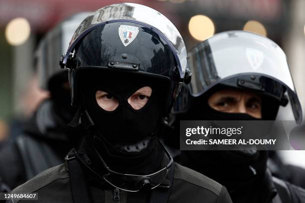 Masked police officers wearing riot helmets stand by during a demonstration after the government pushed a pensions reform through parliament without...