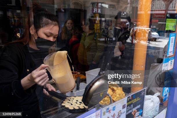 View through a Chinese restaurant window as customers queue up while a chef pours mixture into a bubble waffle maker in Chinatown on 27th March 2023...