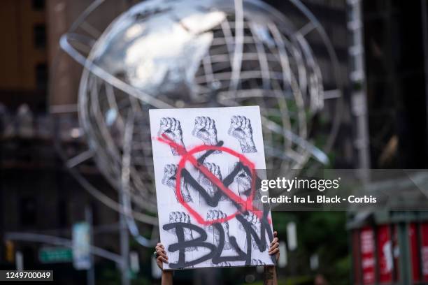 Protester wearing a mask holds a homemade sign that says, "BLM" with a swastika in a circle with a line through it and a pattern of Black Power fists...