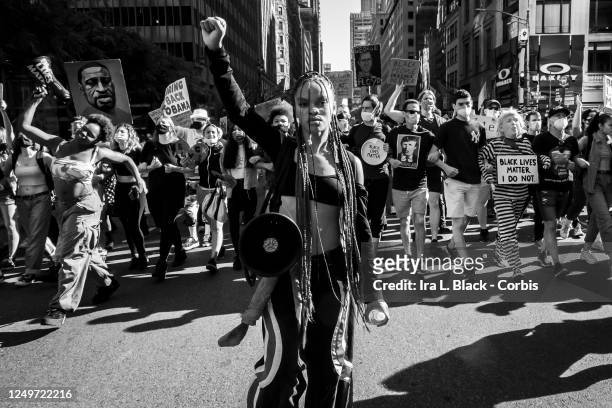 Black and white version of Livia Johnson, an organization leader for Warriors in the Garden holds a up her hand in a raised fist as she stands in...