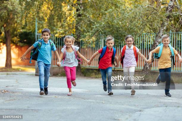 schulkinder halten hände und laufen gemeinsam zur schule - schulbeginn stock-fotos und bilder