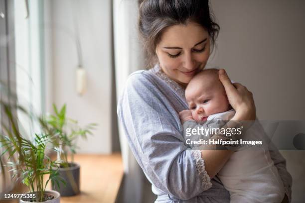 loving and affectionate mother holding newborn baby indoors at home. - mothers babies fotografías e imágenes de stock