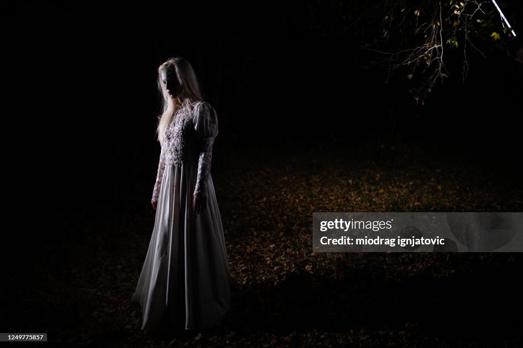 Mujer joven con traje de persona de miedo para Halloween en el bosque durante la noche