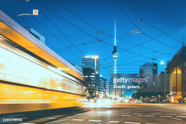 yellow street cars crossing intersection in front of berlin tv-tower  at blue hour - berlin stock pictures, royalty-free photos & images
