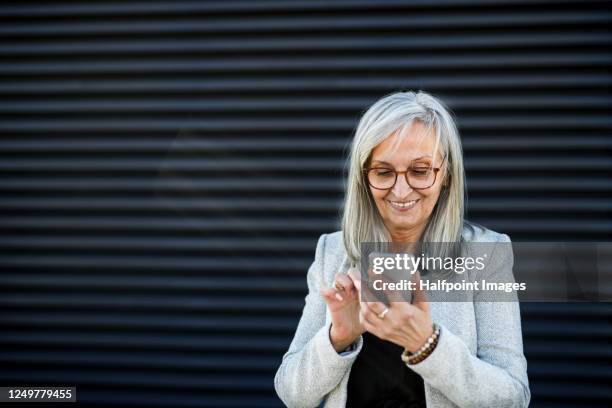 portrait of senior businesswoman standing outdoors on terrace, using smartphone. - senior man grey long hair stock-fotos und bilder