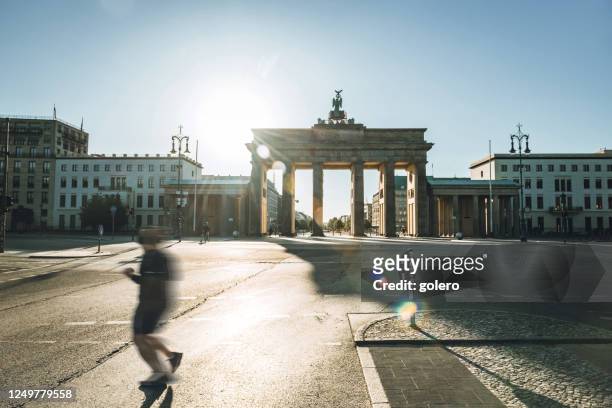 runner passing in front of brandenbuger tor in berlin in the morning light - berlin stock pictures, royalty-free photos & images