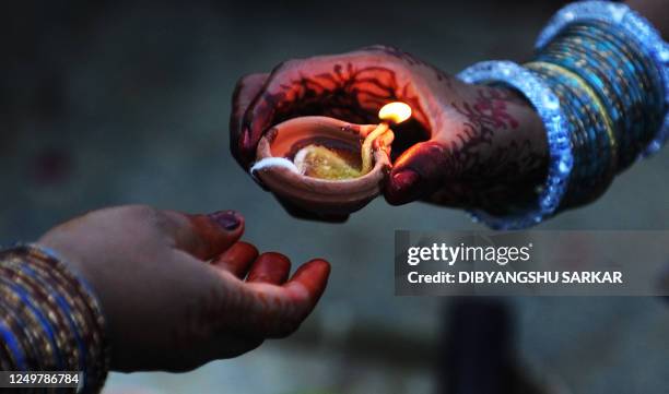 An Indian Hindu devotee hand over a traditional oil lamp as they prepare for prayers to the sun during the Chhath Festival while standing in a water...