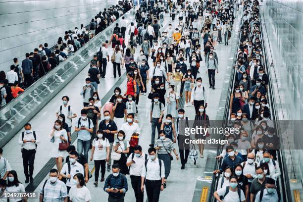 crowd of busy commuters with protective face mask walking through platforms at subway station during office peak hours in the city - epidemie stock-fotos und bilder