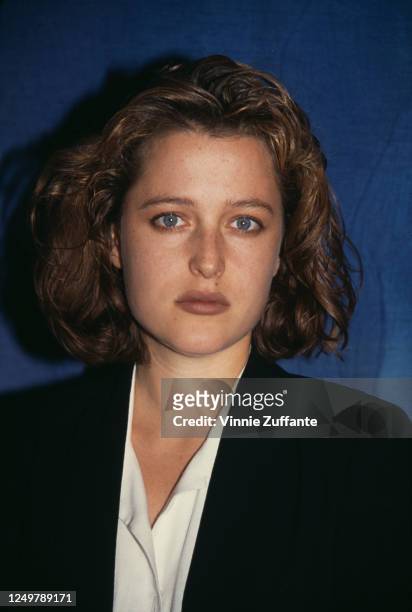 American-British actress Gillian Anderson, wearing a black jacket with a white blouse, poses against a blue background, 1993.