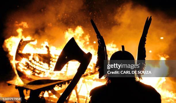 The Guizer Jarl or Chief of the Jarl viking squad is silhoutted by a burning viking longship during the annual Up Helly Aa Festival, Lerwick,...