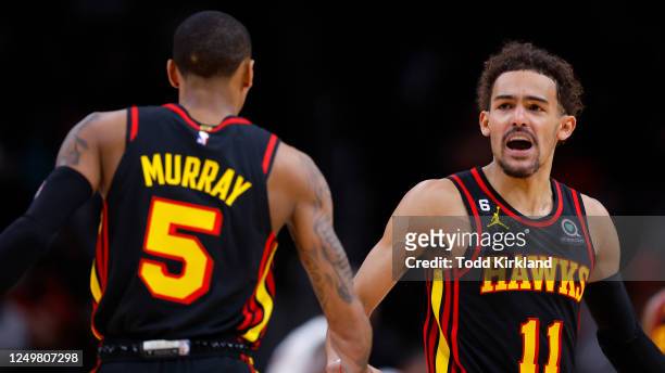 Trae Young reacts with Dejounte Murray of the Atlanta Hawks during the first half against the Cleveland Cavaliers at State Farm Arena on March 28,...