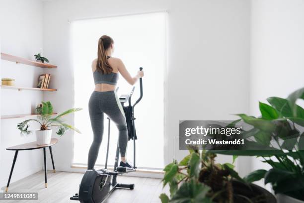 woman performing workout on elliptical trainer at home - cross trainer stock-fotos und bilder