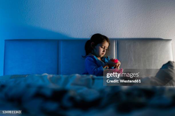 little girl sitting on bed playing with her toy - girl bedroom stock pictures, royalty-free photos & images