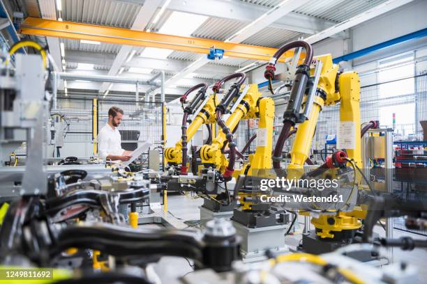 young engineer reading paper while standing by robotic arms in automated industry - evolution of the robot stock pictures, royalty-free photos & images