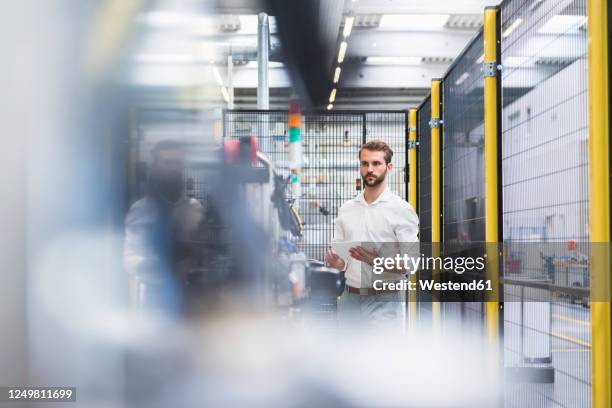 young male engineer standing with digital tablet while looking away at manufacturing industry - factory ipad stock-fotos und bilder