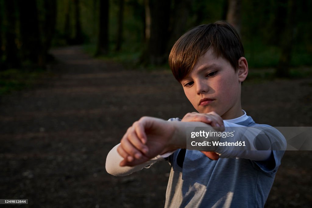 Boy rolling sleeve while standing in forest