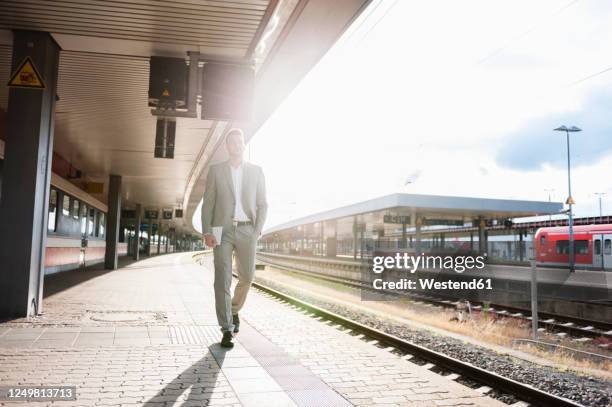 young businessman walking on station platform in backlight - grey suit stock-fotos und bilder