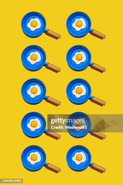 pattern of rows of fried eggs on blue pans against yellow background - frying egg stock illustrations