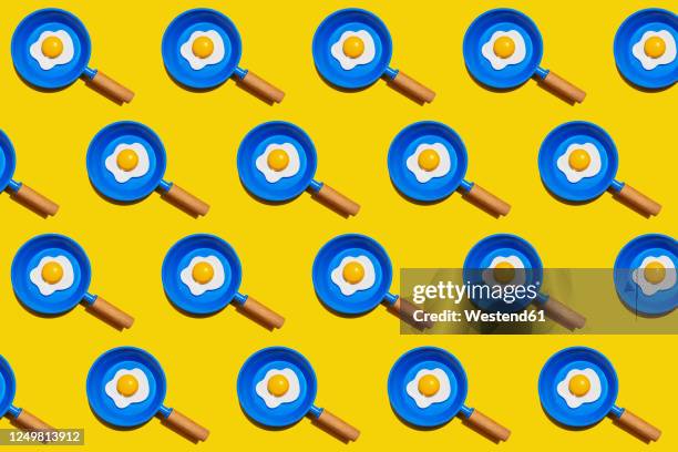 pattern of rows of fried eggs on blue pans against yellow background - food stock illustrations