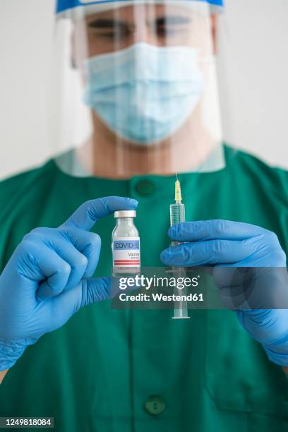 man in protective wear holding covid-19 vaccine and syringe - person wearing vaccine sticker stock pictures, royalty-free photos & images