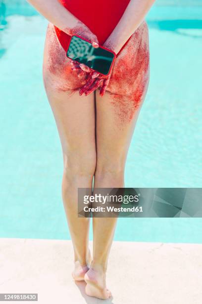 rear view of woman holding cell phone with bottom covered with red sand - pool of blood stock-fotos und bilder