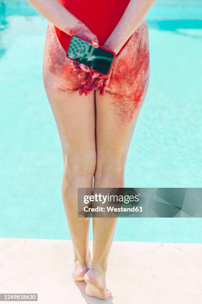 rear view of woman holding cell phone with bottom covered with red sand - period blood foto e immagini stock