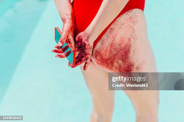 rear view of woman holding cell phone with bottom covered with red sand - red blood cells photos et images de collection