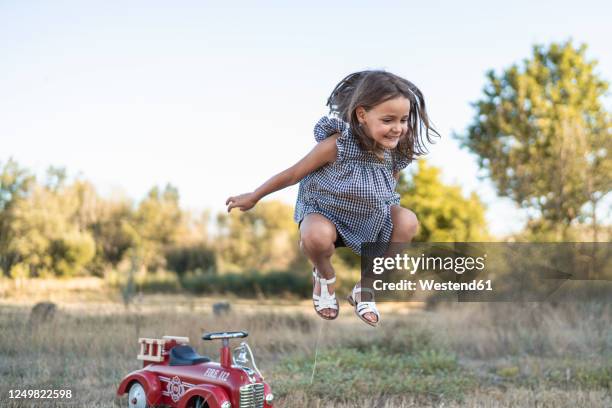 portrait of little girl jumping in the air in nature - bobbycar stockfoto's en -beelden