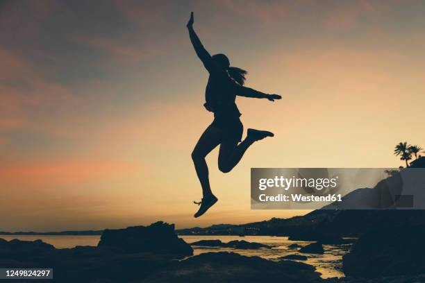 silhouette of jumping woman at beach during sunset - woman leaping silhouette stock pictures, royalty-free photos & images