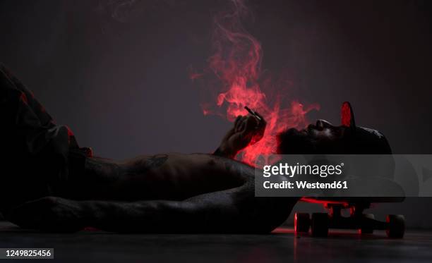 tattooed skateboarder lying on the floor smoking a joint - marijuana tattoo stock pictures, royalty-free photos & images