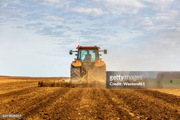 back view of farmer in tractor plowing field in spring - ploughed field stock pictures, royalty-free photos & images
