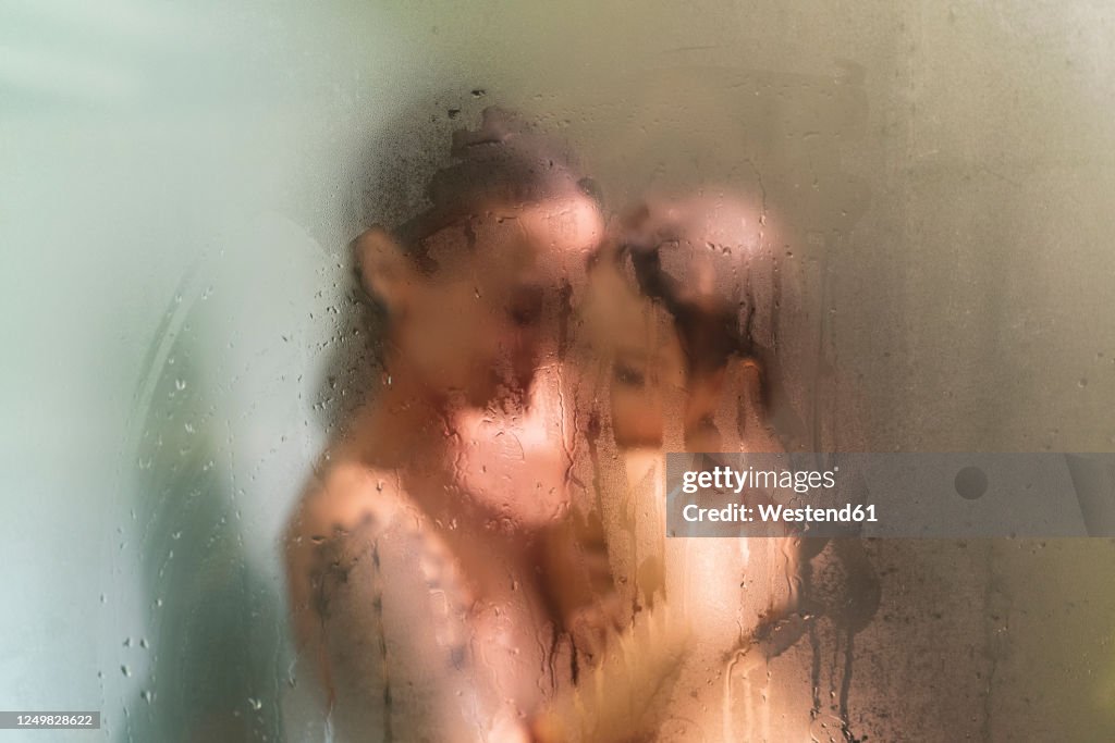 Daughter in mother's arms in the shower behind wet glass