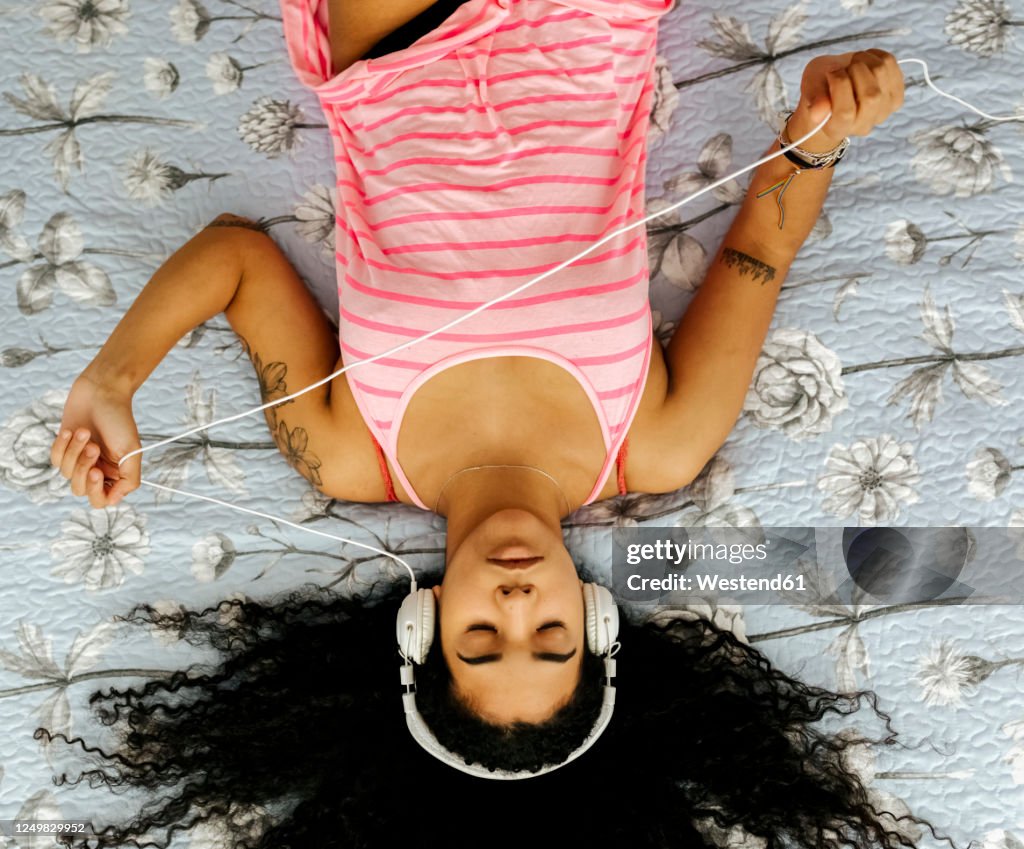 Top view of beautiful young woman lying on bed at home listening to music