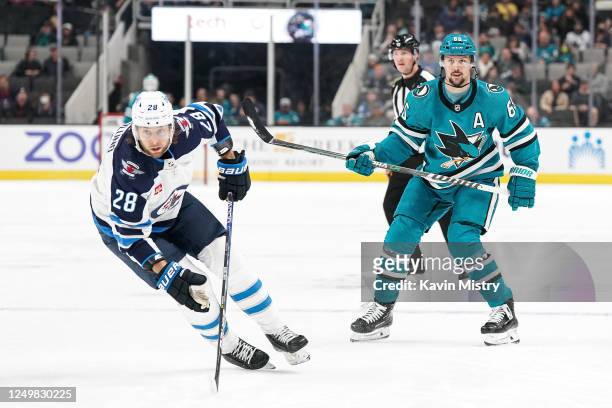 Erik Karlsson of the San Jose Sharks passes the puck ahead in the first period against Kevin Stenlund of the Winnipeg Jets at SAP Center on March 28,...
