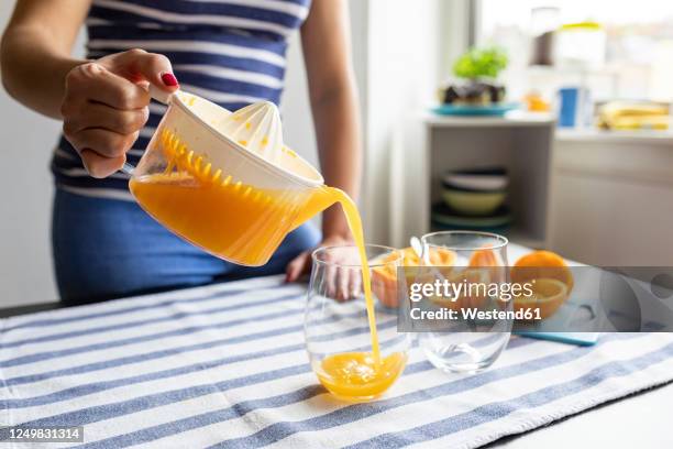 woman pouring freshly sqeezed orange juice into glasses - saftpresse stock-fotos und bilder