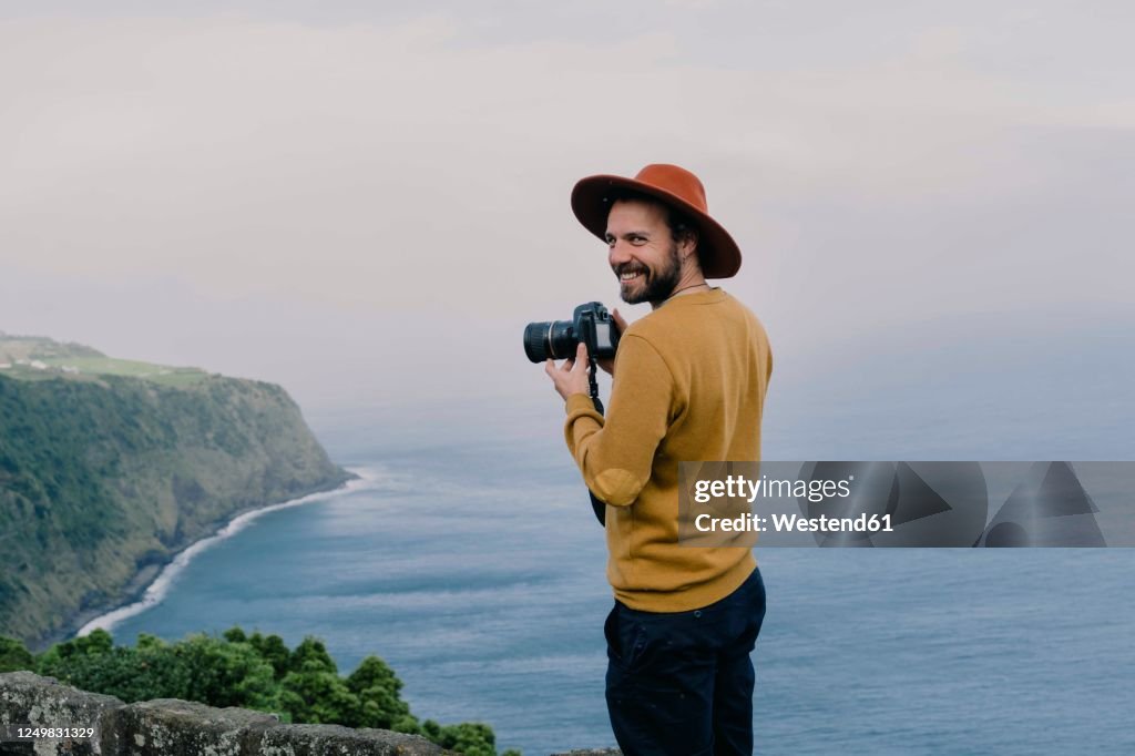 Smiling man with a camera at the coast on Sao Miguel Island, Azores, Portugal