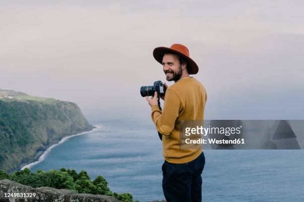smiling man with a camera at the coast on sao miguel island, azores, portugal - tourist stock-fotos und bilder