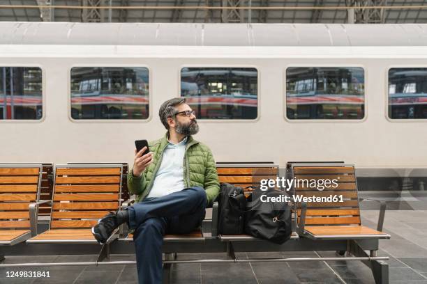 man sitting on a bench at the train station - train platform photos et images de collection