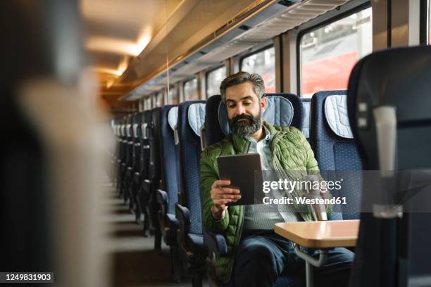 man sitting in train using tablet - tren de pasajeros fotografías e imágenes de stock