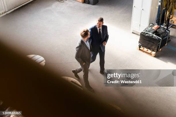 bird's eye view of two businessmen walking and talking in a factory - business man walk stock-fotos und bilder