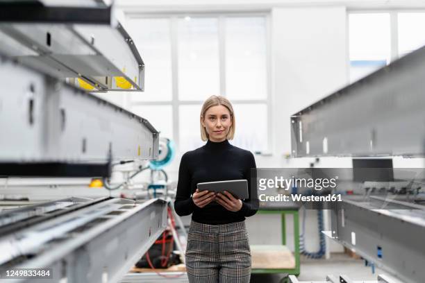 woman holding tablet at metal rods in factory hall - herstellendes gewerbe stock-fotos und bilder