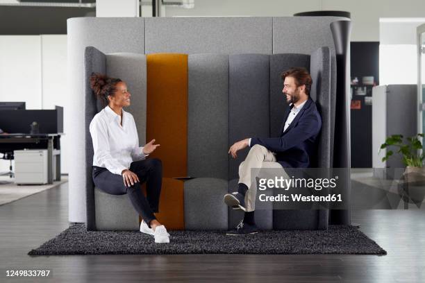 colleagues keeping distance while talking together in office - sitzen stock-fotos und bilder