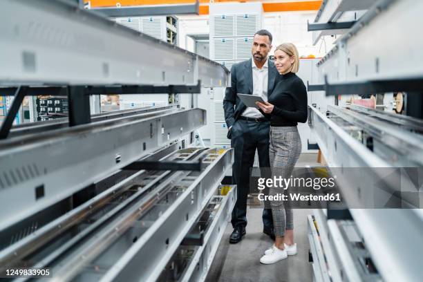 businessman and woman with tablet at metal rods in factory hall - building shelves stock-fotos und bilder