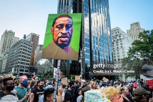 Hundreds of people pack into Columbus Circle to hear speeches against police violence while one of them holds a painted portrait of George Floyd in...