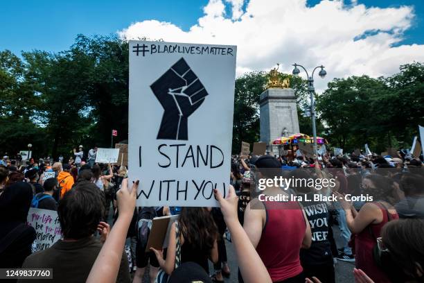 Protester holds a homemade sign above their head that says, "I Stand With You" with a Black Power raised fist on the sign and #blacklivesmatter in...